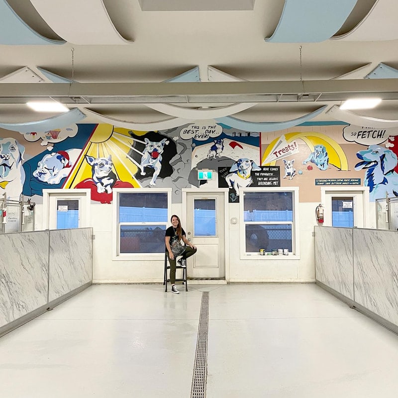 Inside the Big Dog Barn: white suites, a staff member on a stool and a comic-book mural of dogs on the wall